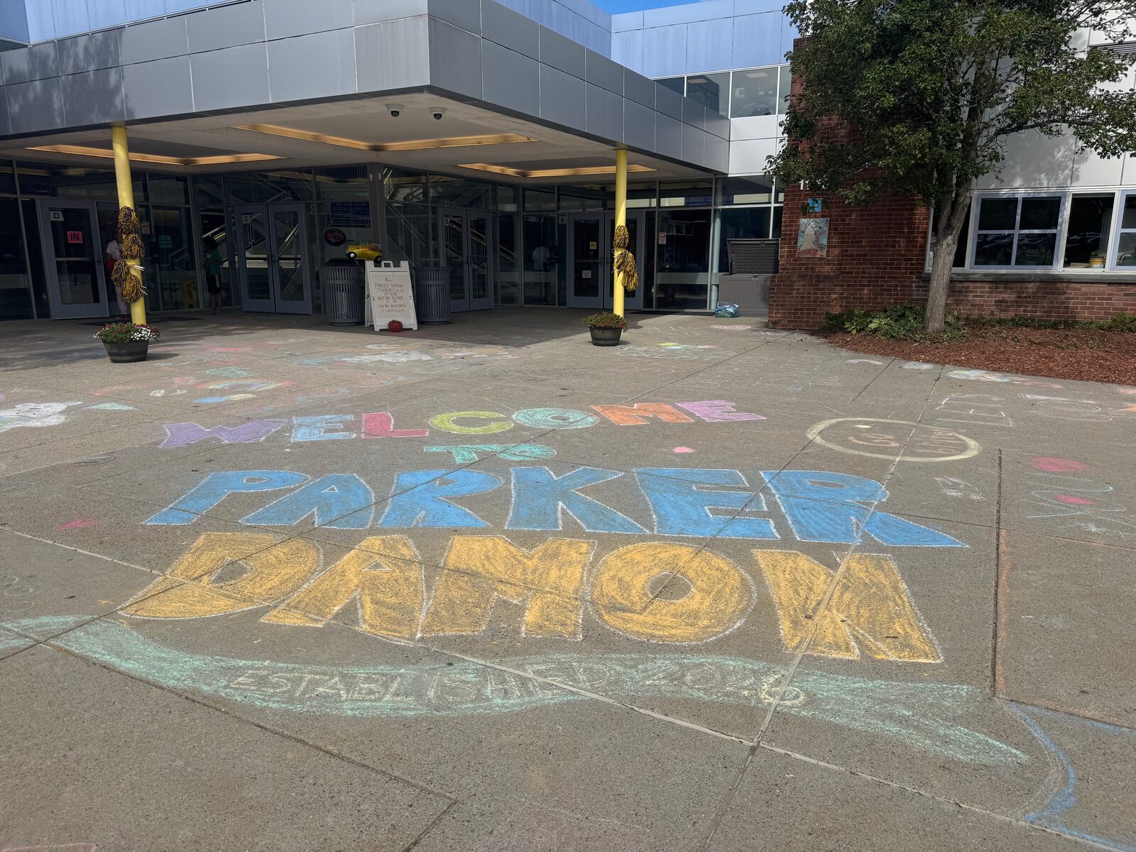 Sidewalk chalk outside the school entrance reading "Welcome to Parker Damon, Established 2026".